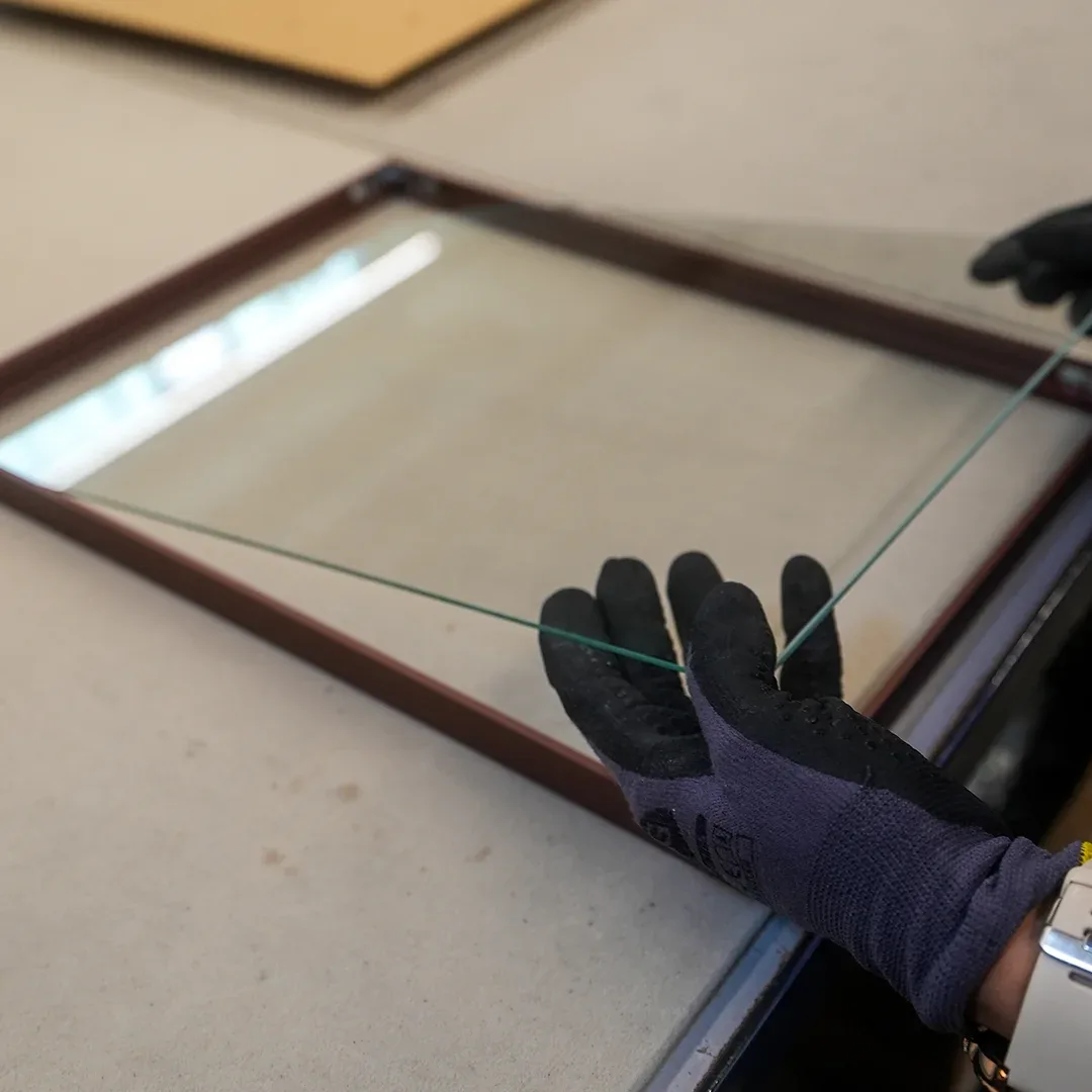 Avec des gants de protection, une plaque de verre est posée dans un cadre en bois foncé