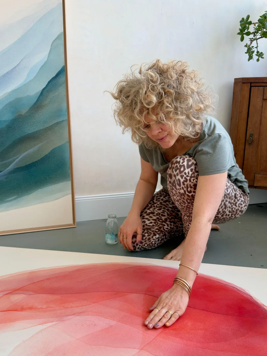 Johanne Bossmann peint à la main sur une toile aux tons rouges, à côté d'une œuvre bleue encadrée