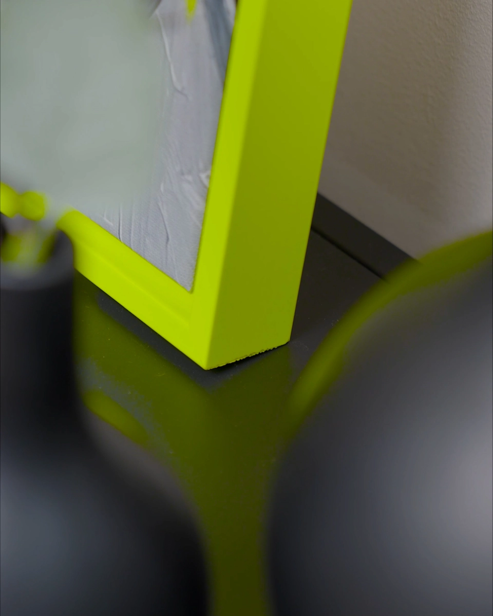 Gros plan sur l’angle du cadre de type caisse américaine Jill en jaune néon éclatant pour toiles, dans un intérieur chaleureux.