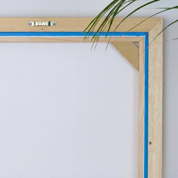 Vue arrière d'un cadre américain avec attache et toile devant un mur beige. Une feuille de palmier est visible en haut.