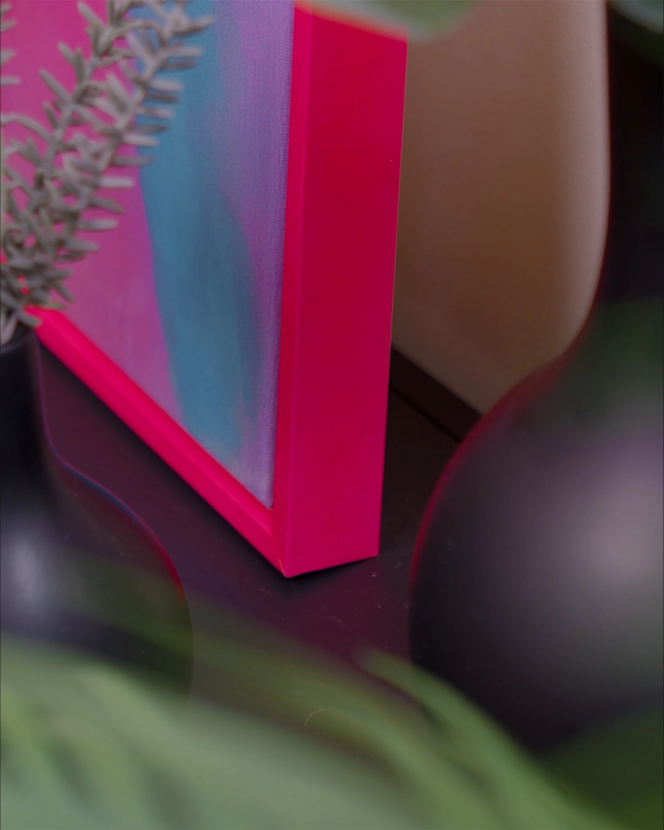 Gros plan sur l’angle du cadre de type caisse américaine Jill en pink néon éclatant pour toiles, dans un intérieur chaleureux.