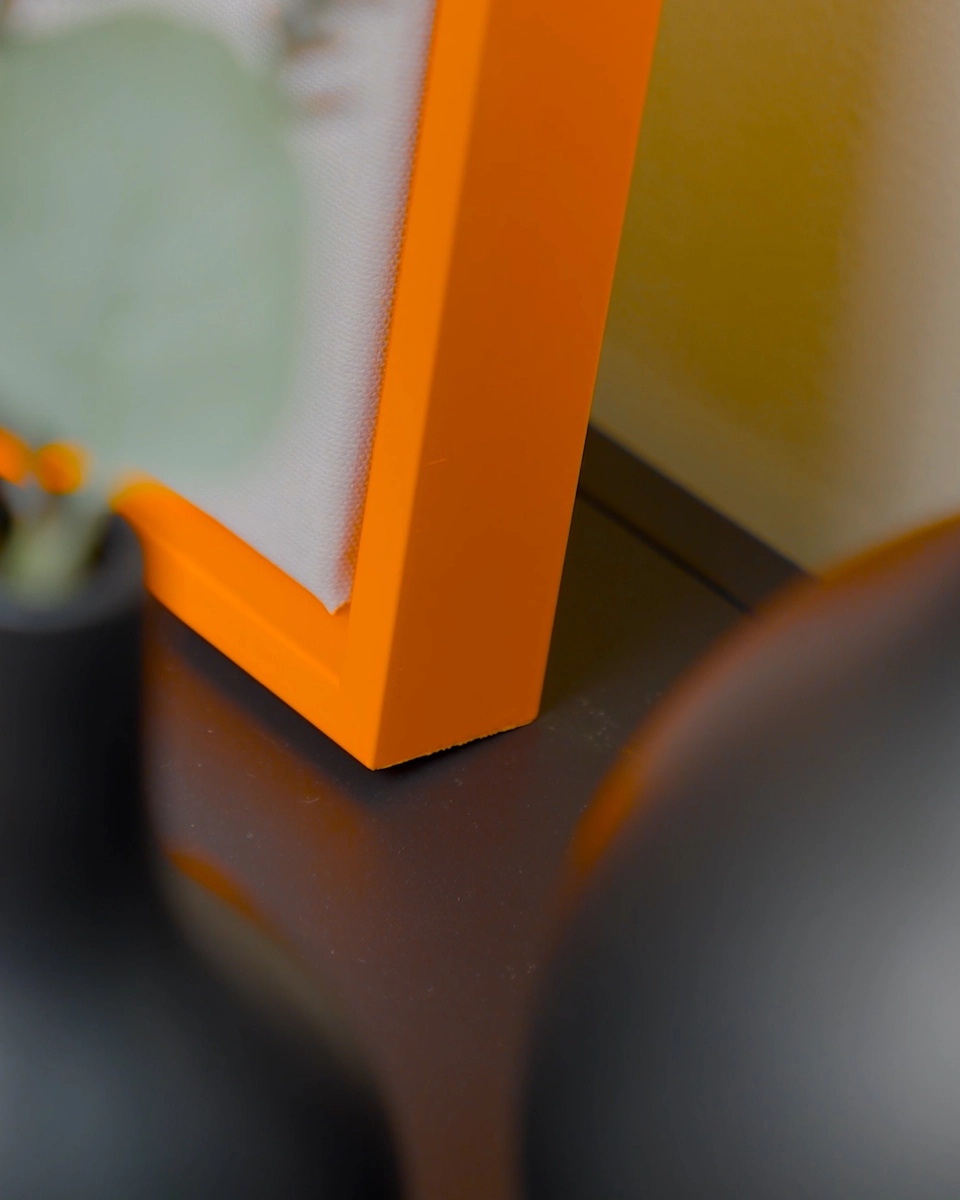 Gros plan sur l’angle du cadre de type caisse américaine Jill en orange néon éclatant pour toiles, dans un intérieur chaleureux.